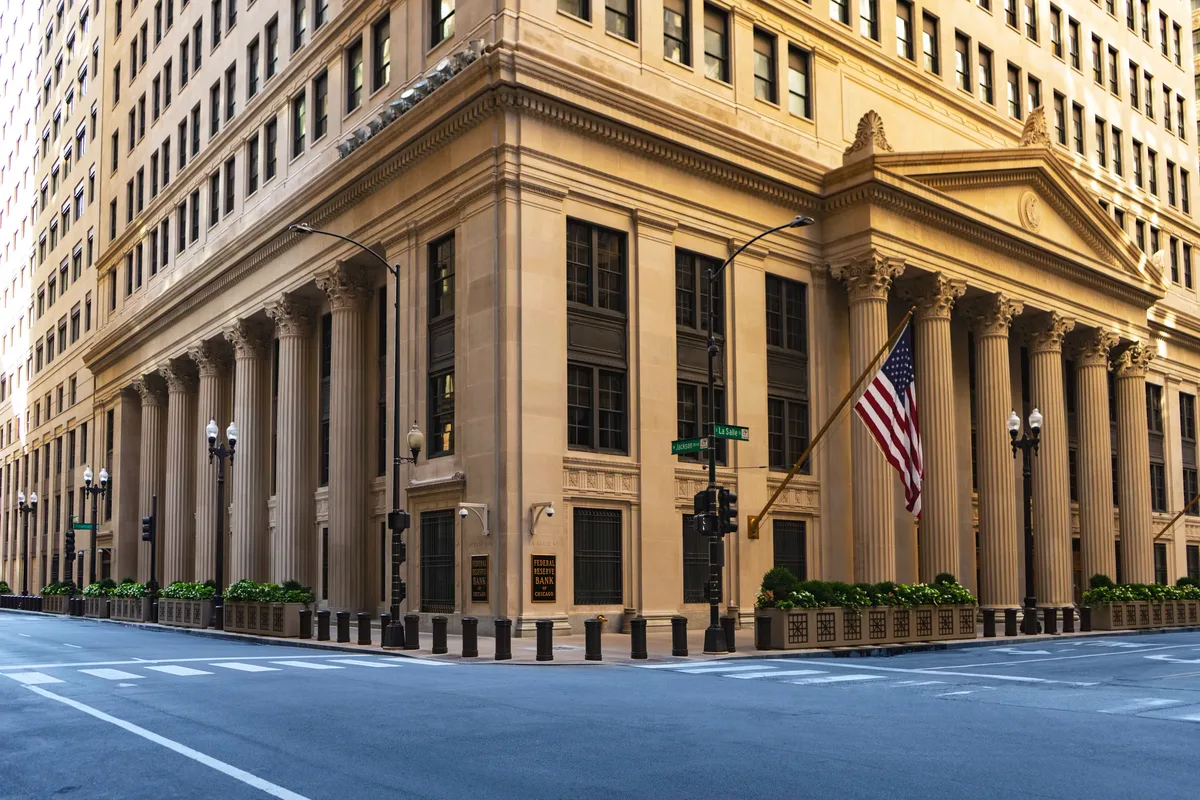 Federal Reserve-style building with columns and an American flag, representing U.S. monetary policy